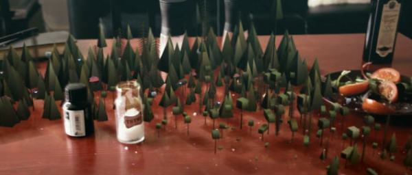 Un bosque en miniatura sobre una mesa, entre frascos y un plato con tomates.
